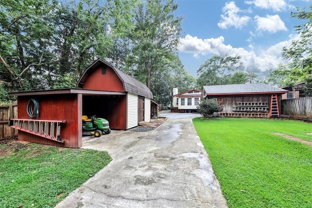 exterior space with concrete driveway, a gambrel roof, fence, an outdoor structure, and a front lawn