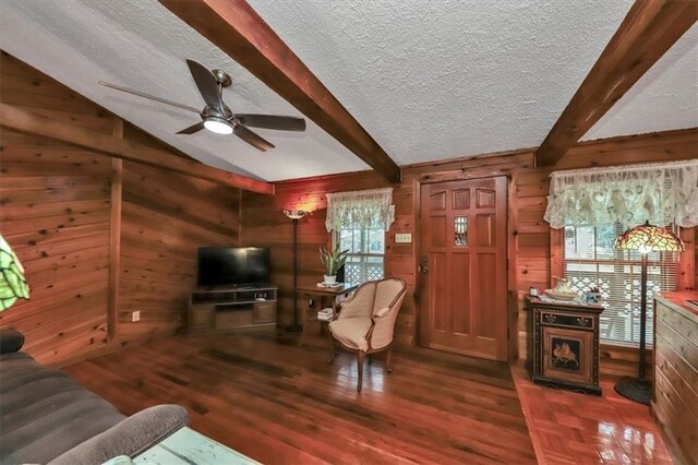 living room with ceiling fan, a textured ceiling, hardwood / wood-style flooring, vaulted ceiling with beams, and wooden walls