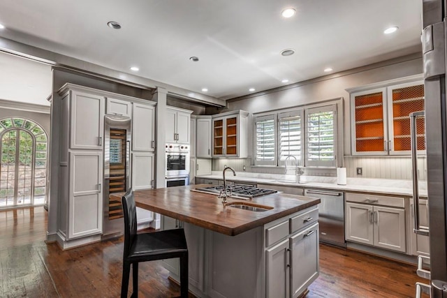 kitchen with a kitchen island with sink, sink, butcher block countertops, dark hardwood / wood-style flooring, and stainless steel appliances