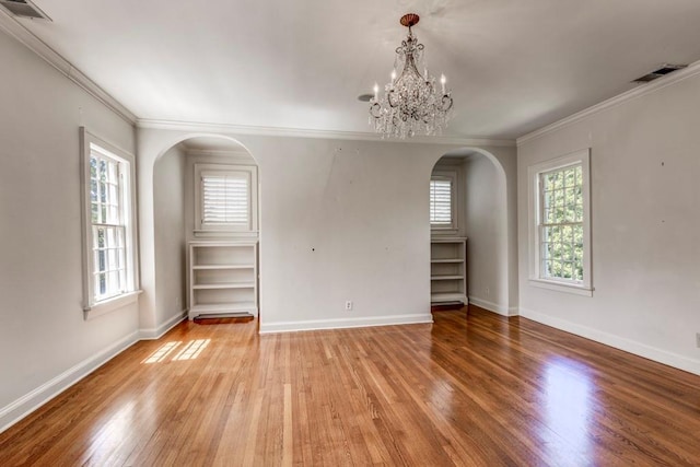 empty room with built in features, light wood-type flooring, ornamental molding, and an inviting chandelier