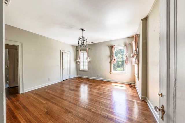 spare room featuring dark wood-type flooring and an inviting chandelier