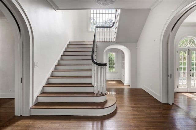 staircase featuring a healthy amount of sunlight, crown molding, wood-type flooring, and a notable chandelier