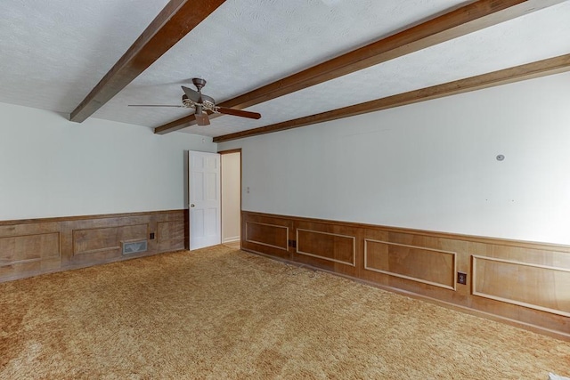 empty room with a textured ceiling, wooden walls, carpet, and beamed ceiling