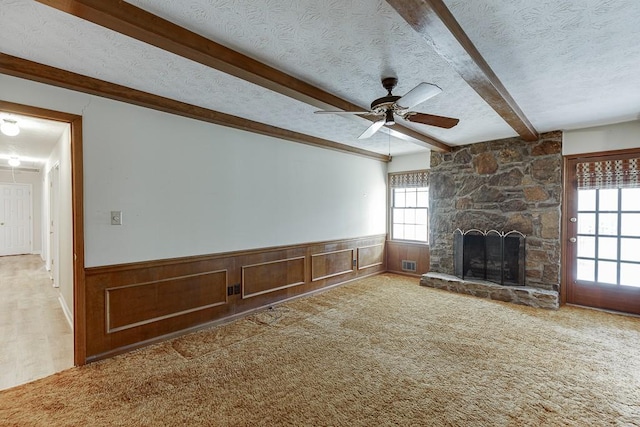 unfurnished living room with a fireplace, a textured ceiling, carpet, beamed ceiling, and ceiling fan