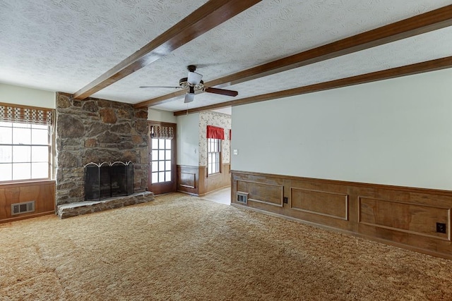 unfurnished living room featuring a fireplace, a textured ceiling, beamed ceiling, ceiling fan, and light carpet