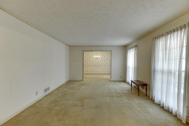 spare room with crown molding, light colored carpet, a textured ceiling, and an inviting chandelier