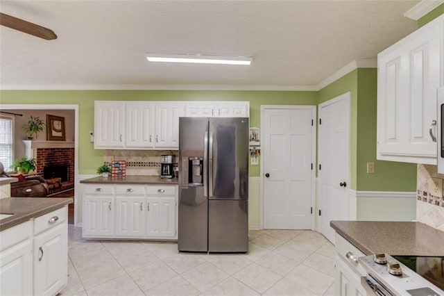 kitchen featuring tasteful backsplash, white cabinets, a ceiling fan, stainless steel fridge with ice dispenser, and a brick fireplace