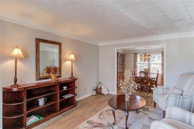 living area with a notable chandelier, light wood-style flooring, ornamental molding, a textured ceiling, and baseboards