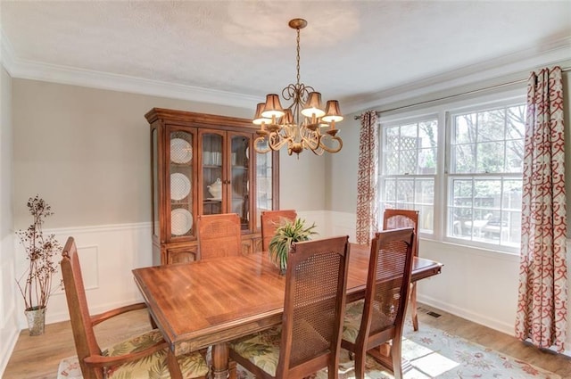 dining space with light wood-type flooring, a wainscoted wall, a notable chandelier, and crown molding