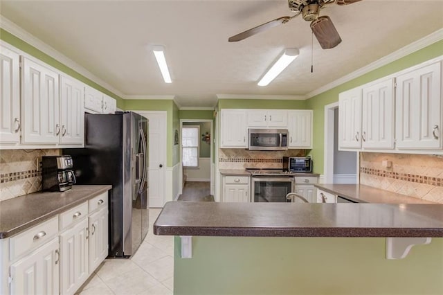 kitchen featuring light tile patterned floors, stainless steel appliances, dark countertops, white cabinetry, and a peninsula