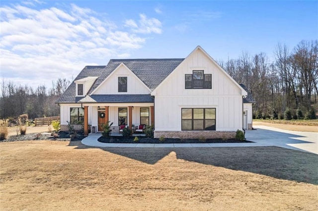 modern farmhouse featuring fence, board and batten siding, covered porch, a front yard, and a shingled roof