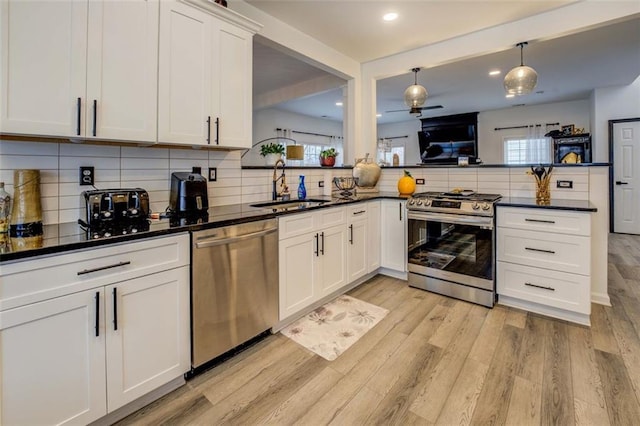 kitchen with appliances with stainless steel finishes, tasteful backsplash, sink, white cabinets, and light hardwood / wood-style flooring