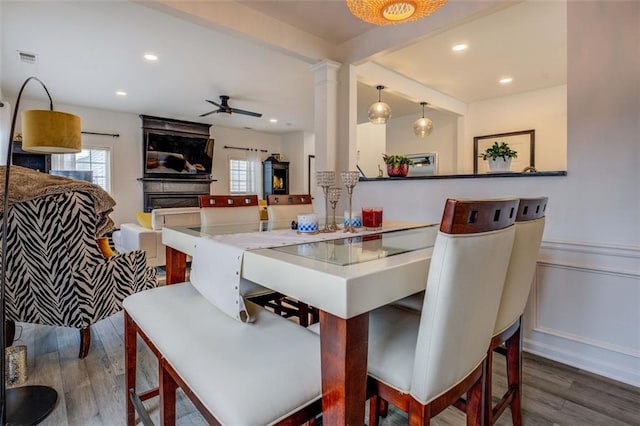 dining space with hardwood / wood-style flooring, ceiling fan, a fireplace, and decorative columns