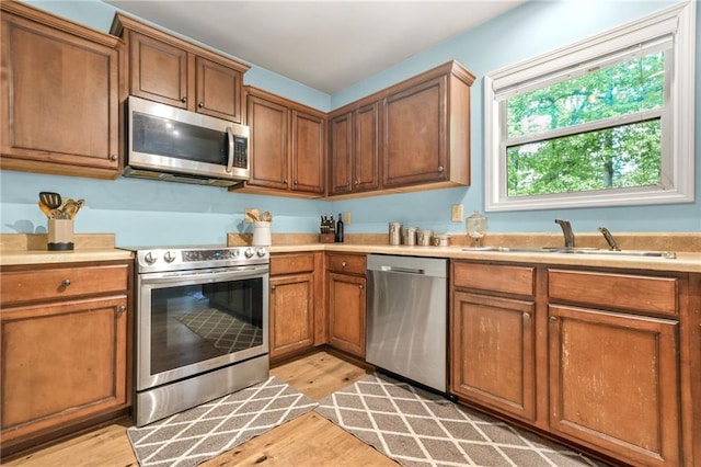 kitchen with appliances with stainless steel finishes, a sink, light wood-style floors, and brown cabinets