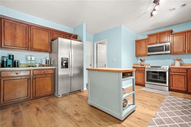 kitchen with stainless steel appliances, brown cabinetry, and light wood-style flooring
