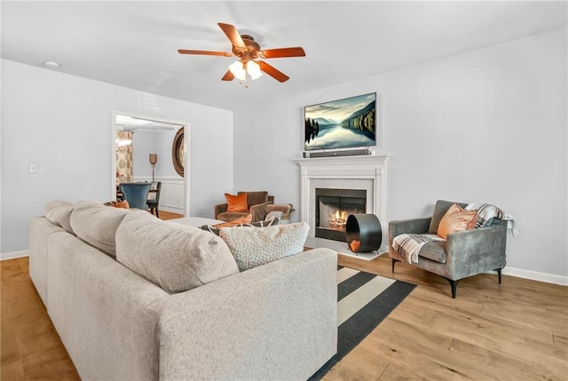 living room featuring a ceiling fan, light wood-style floors, a fireplace with flush hearth, and baseboards