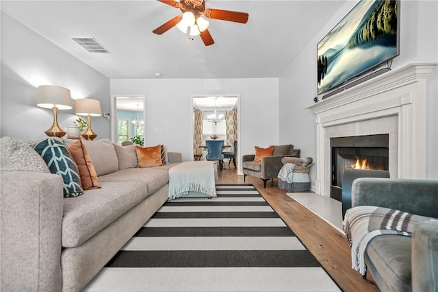 living room with wood finished floors, a chandelier, a ceiling fan, and a lit fireplace