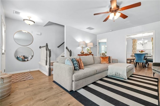 living area featuring light wood finished floors, ceiling fan, a chandelier, stairway, and baseboards