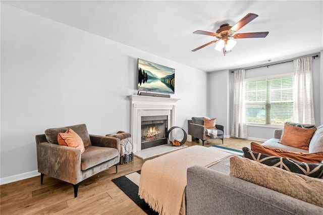 living area featuring a lit fireplace, a ceiling fan, baseboards, and light wood-style floors