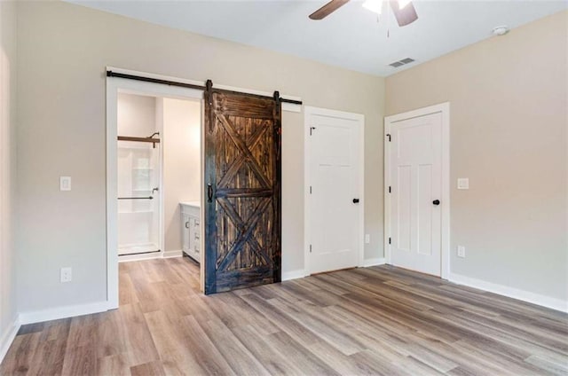 12 New St, Newnan, GA 30263 - unfurnished bedroom featuring a barn door, light wood finished floors, baseboards, connected bathroom, and ceiling fan