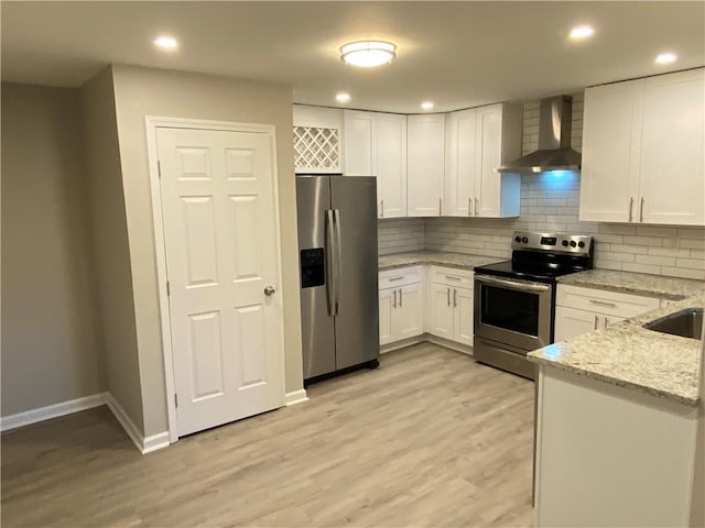 kitchen featuring light stone countertops, wall chimney exhaust hood, stainless steel appliances, white cabinets, and light hardwood / wood-style floors