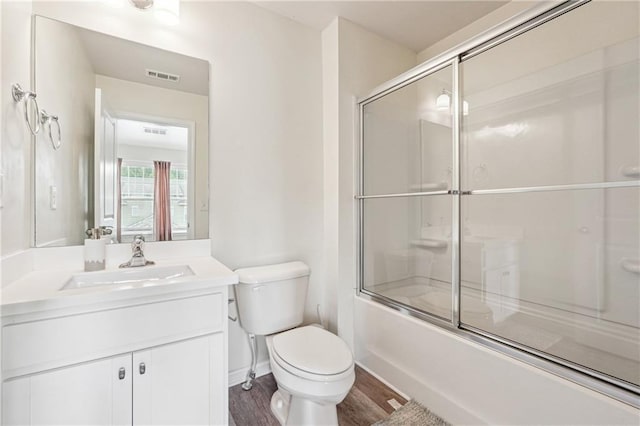 full bathroom featuring wood-type flooring, vanity, toilet, and bath / shower combo with glass door