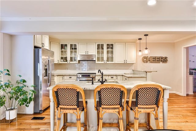 kitchen featuring hanging light fixtures, stainless steel appliances, a kitchen breakfast bar, light hardwood / wood-style floors, and light stone countertops