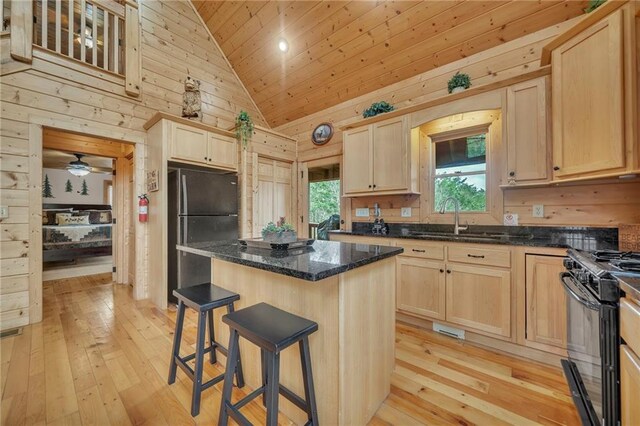 kitchen featuring a kitchen island, dark stone counters, sink, black appliances, and high vaulted ceiling