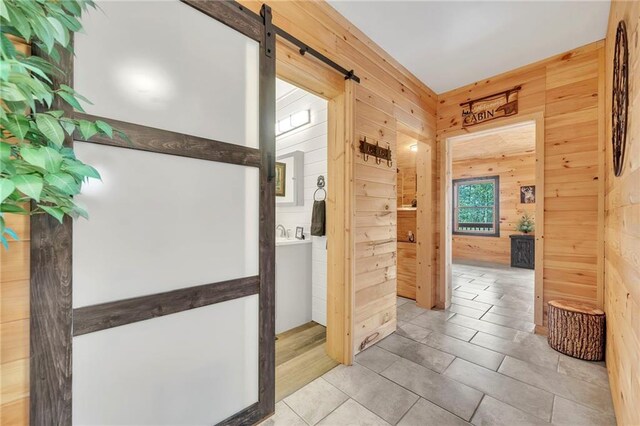 hallway with a barn door, wooden walls, and light tile patterned floors