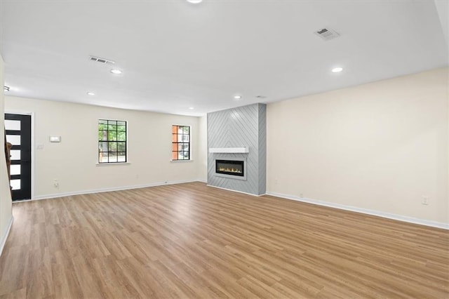 unfurnished living room featuring a large fireplace, light wood-style flooring, visible vents, and baseboards