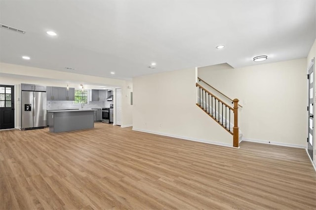 unfurnished living room with light wood-type flooring, visible vents, baseboards, and stairs