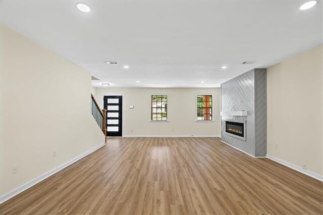 unfurnished living room featuring baseboards, light wood-style flooring, stairs, a fireplace, and recessed lighting