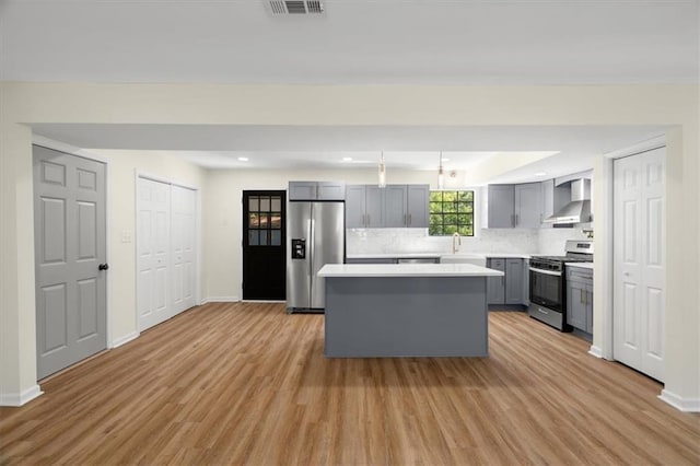 kitchen featuring gray cabinets, light countertops, appliances with stainless steel finishes, a kitchen island, and wall chimney exhaust hood