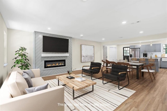 living room featuring light wood-style flooring, a fireplace, visible vents, and recessed lighting