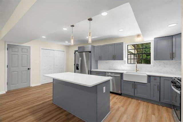 kitchen featuring a kitchen island, a sink, appliances with stainless steel finishes, gray cabinets, and light wood finished floors