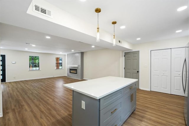 kitchen featuring visible vents, gray cabinetry, dark wood-type flooring, a large fireplace, and a kitchen island