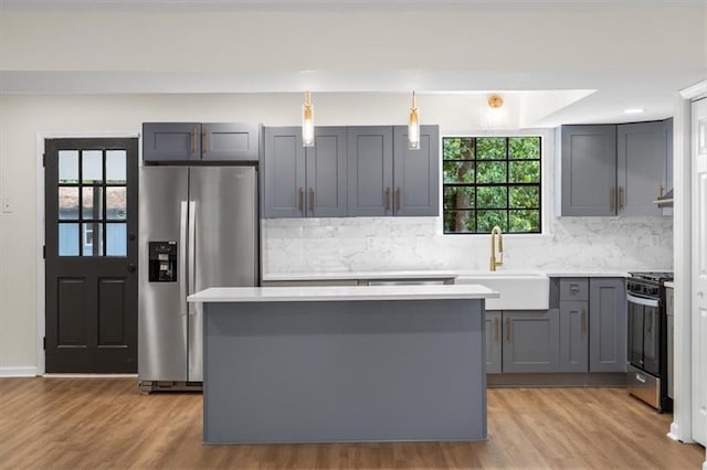 kitchen with gray cabinetry, a sink, light countertops, stainless steel refrigerator with ice dispenser, and gas range oven