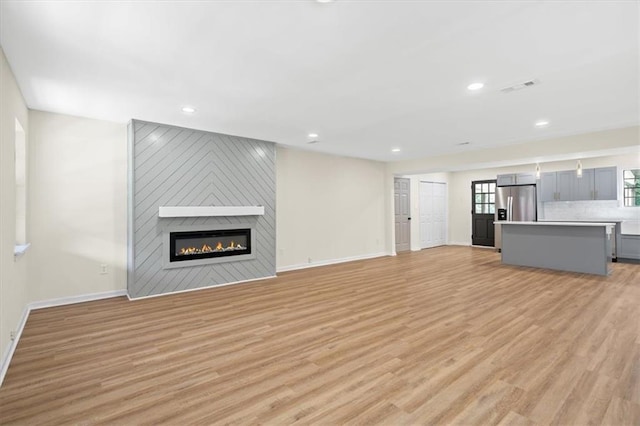 unfurnished living room with a large fireplace, baseboards, visible vents, and light wood finished floors