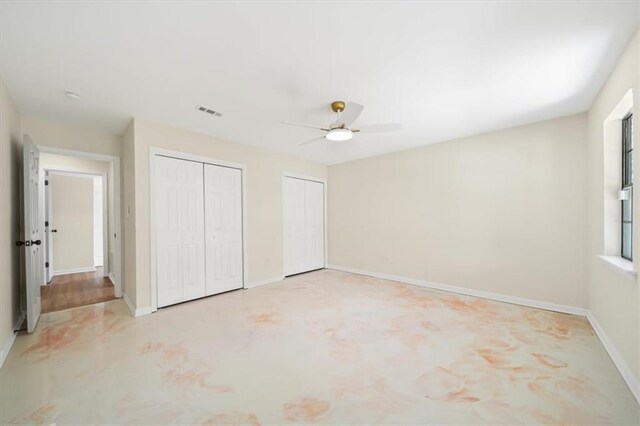 unfurnished bedroom featuring baseboards, ceiling fan, visible vents, and multiple closets