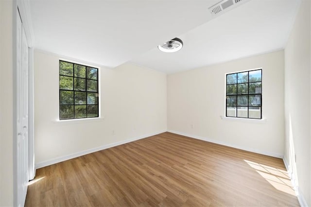 empty room with wood finished floors, visible vents, and baseboards