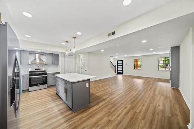 kitchen with light wood-style flooring, stainless steel appliances, light countertops, wall chimney range hood, and gray cabinets