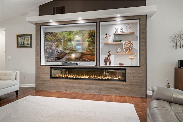 interior space featuring wood finished floors, a glass covered fireplace, visible vents, and baseboards