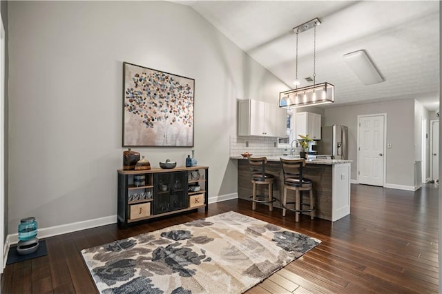 kitchen featuring lofted ceiling, a peninsula, a breakfast bar, dark wood-style flooring, and stainless steel fridge with ice dispenser