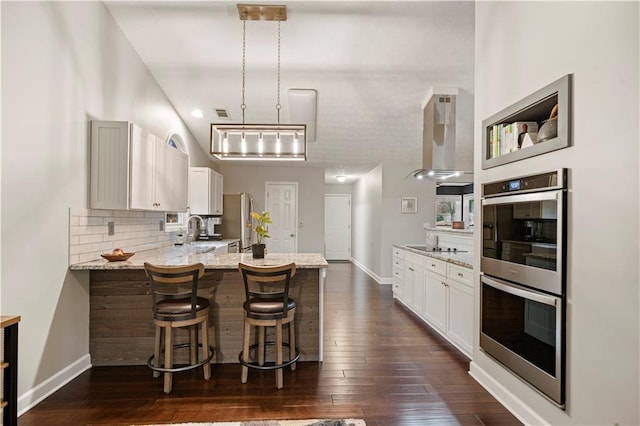 kitchen with decorative backsplash, dark wood-style floors, wall chimney exhaust hood, a peninsula, and double oven