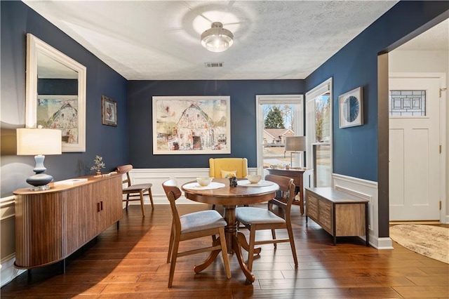 dining area featuring a wainscoted wall, hardwood / wood-style flooring, a textured ceiling, and visible vents