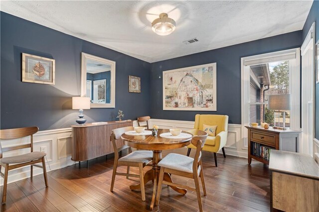 dining space featuring dark wood-type flooring, a wainscoted wall, visible vents, and a textured ceiling