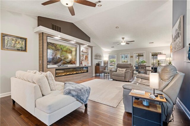 living room featuring visible vents, vaulted ceiling, dark wood-type flooring, and a glass covered fireplace