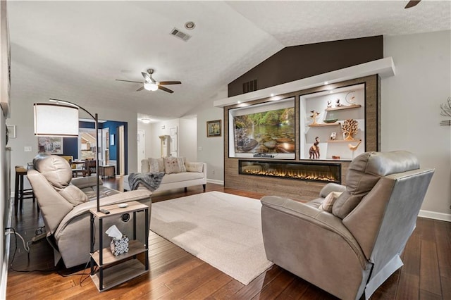 living room featuring visible vents, dark wood finished floors, a ceiling fan, a glass covered fireplace, and vaulted ceiling