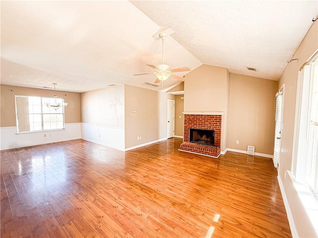 unfurnished living room with lofted ceiling, a brick fireplace, a textured ceiling, hardwood / wood-style floors, and ceiling fan with notable chandelier