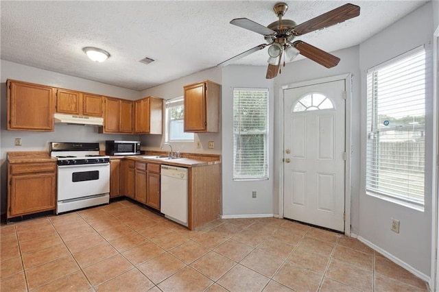 kitchen featuring a textured ceiling, a wealth of natural light, light tile patterned floors, and white appliances